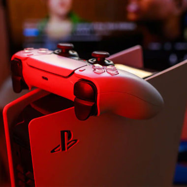 Konsola PlayStation 5 z kontrolerem DualSense w odbiciu czerwonego światła.