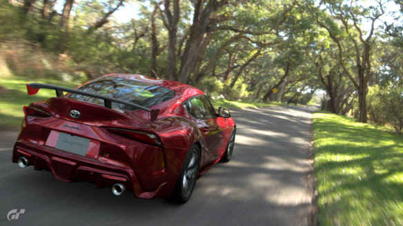 Gran Turismo 7 - czerwone auto jedzie przez drogę wśród drzew - screen zrobiony w trybie fotograficznym