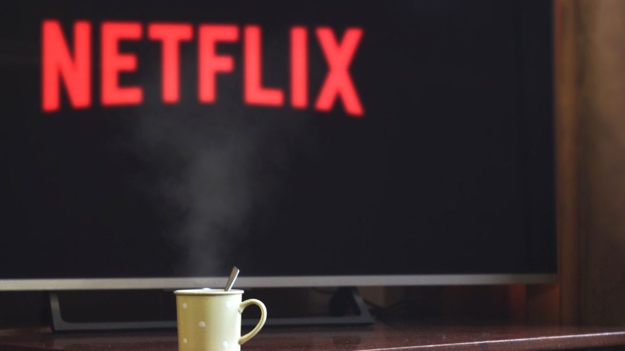 parujący kubek przed telewizorem z logo Netflix