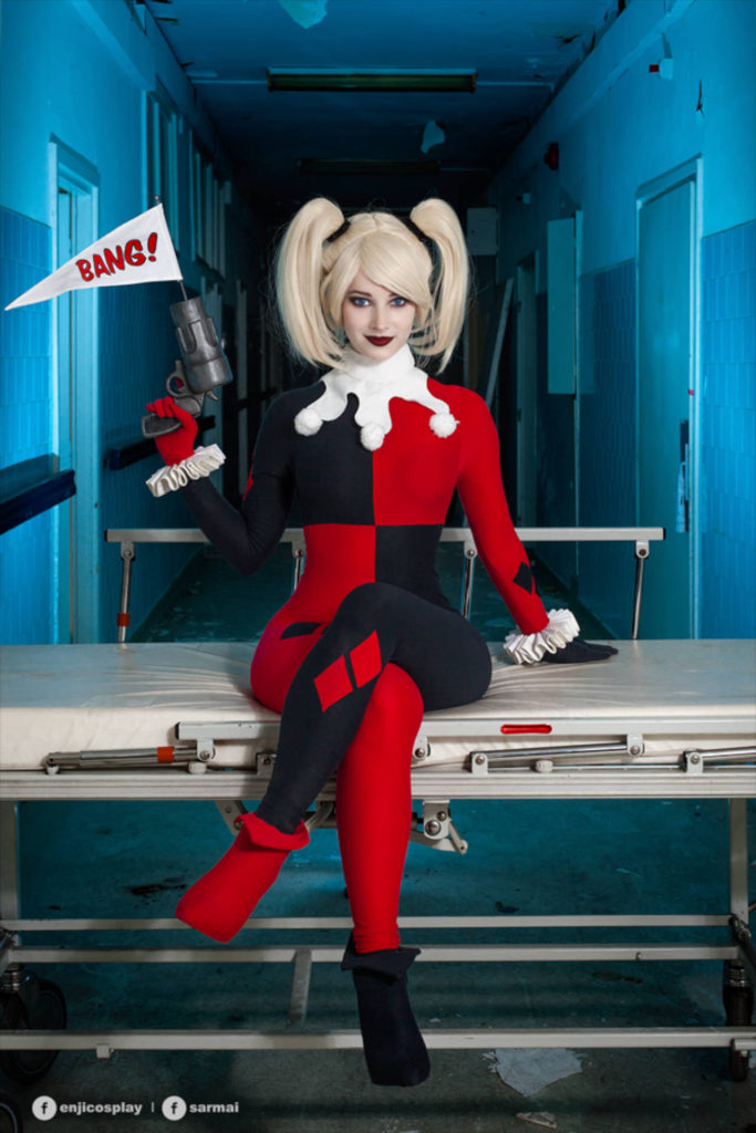 Cosplayerka przebrana za Harley Quinn siedzi z pistoletem, z którego wystaje chorągiewka z napisem "bang"