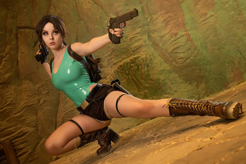 Lara Croft - cosplay - Disharmonica - cosplayerka przykuca na jednej nodze i celuje z pistoletu