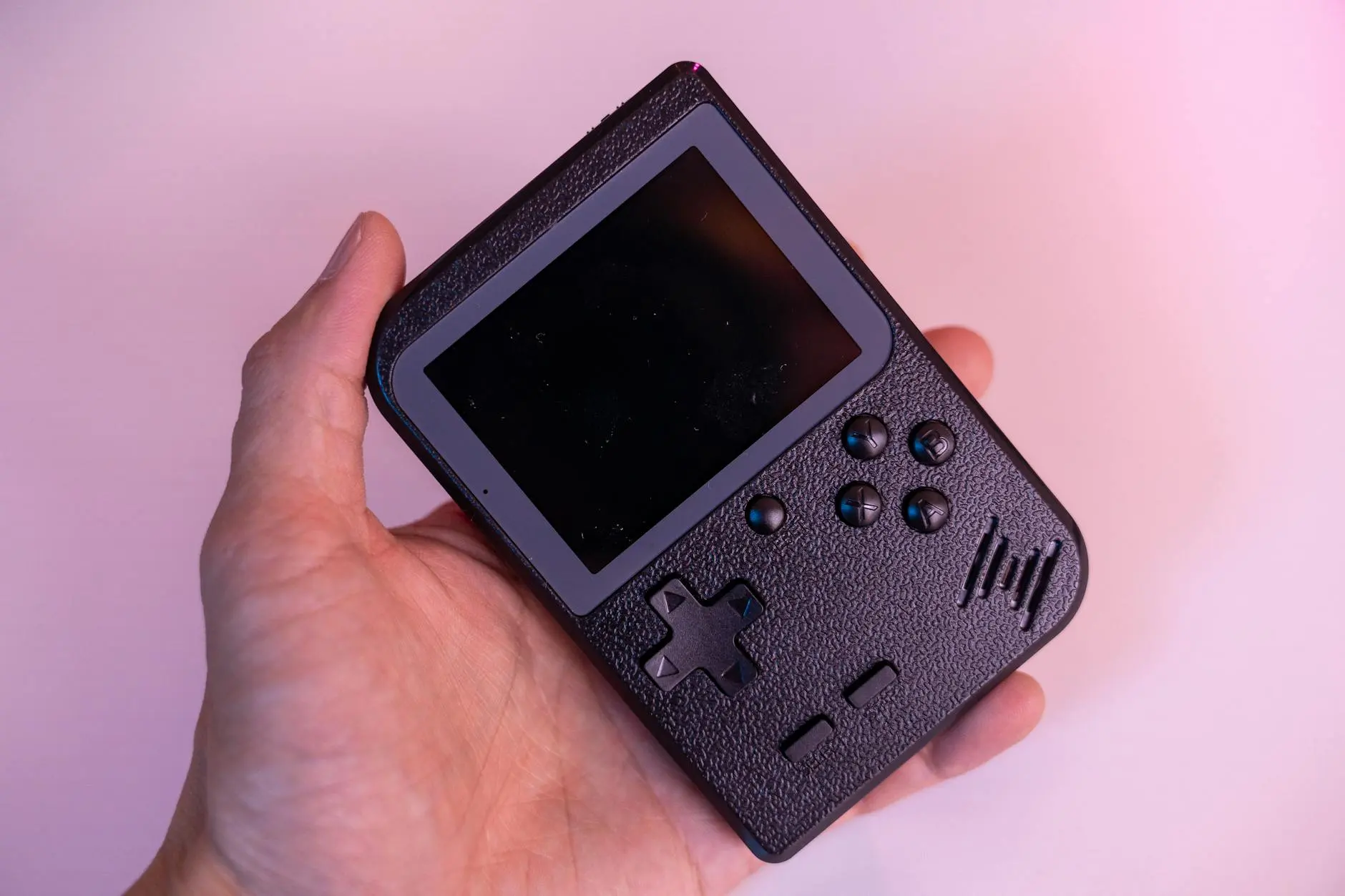 A hand holding a retro gaming handheld emulation console with buttons and a screen.