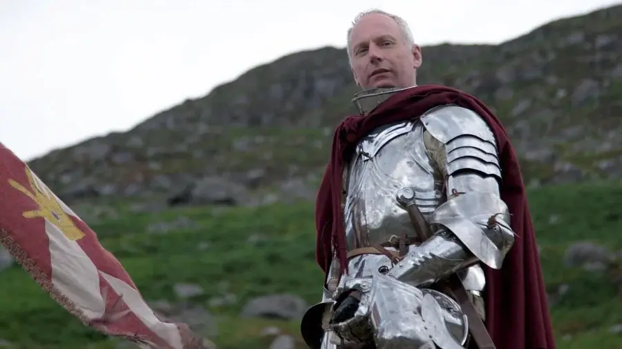 Swen Vincke of Larian Studios wearing a suit of plate armor and a red cape in a hilly landscape