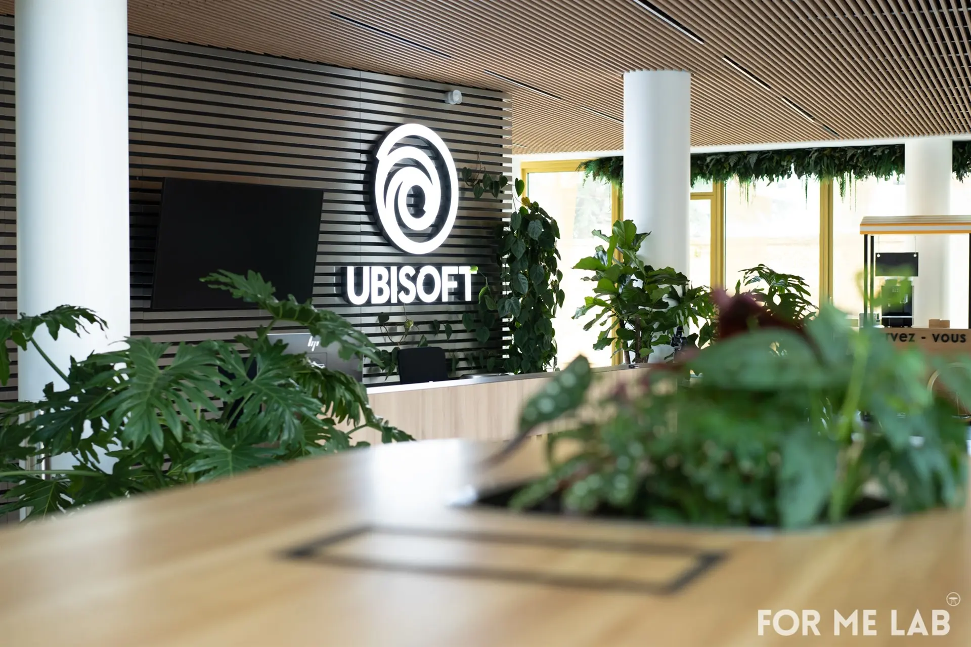 Ubisoft logo displayed in a modern office lobby with plants and wooden elements.